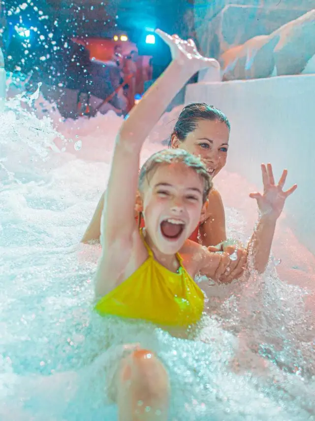 Two smiling children in a swimming pool, one holding a yellow toy