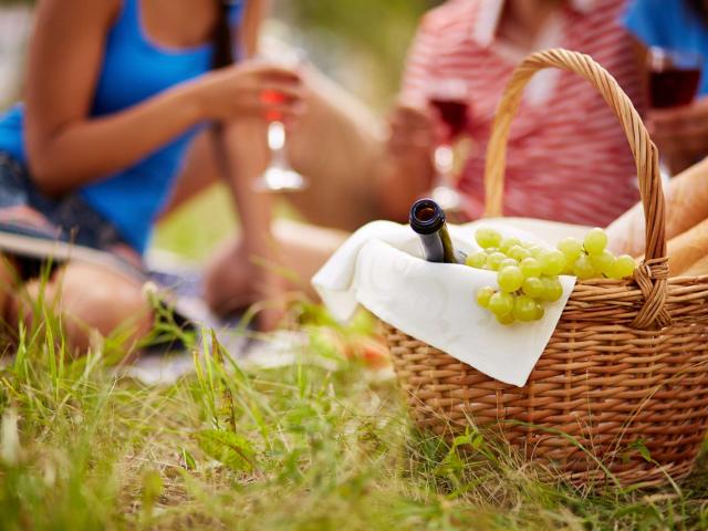 Basket with bottle, bread and grapes on background of cheering friends