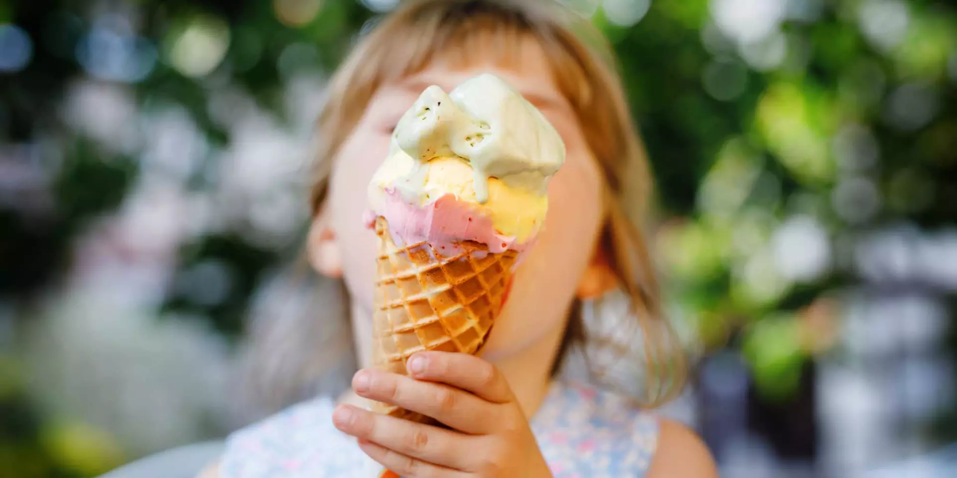 Little preschool girl eating ice cream in waffle cone on sunny summer day. Happy toddler child eat icecream dessert. Sweet food on hot warm summertime days. Bright light, colorful ice-cream.